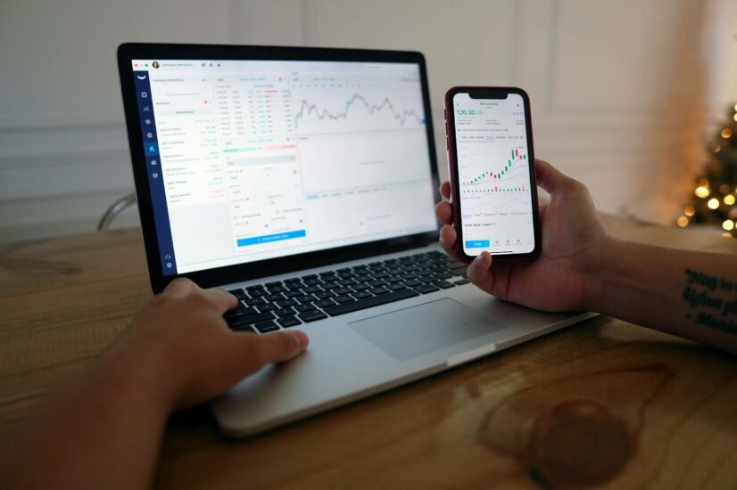 A person examines a laptop and phone screen with data analytics displayed.