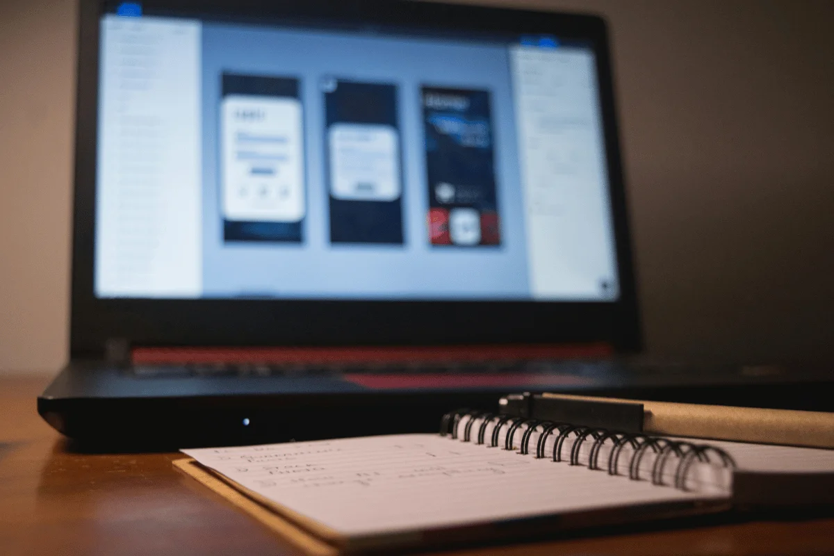 Laptop displaying app design mockups with a notebook in the foreground.